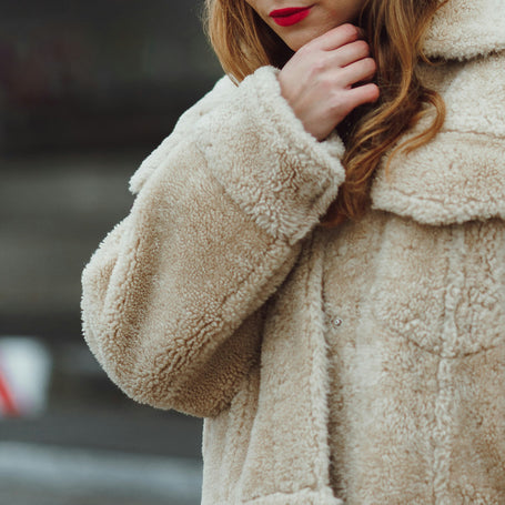 Close-up of a person wearing a beige sherpa coat with a blurred background