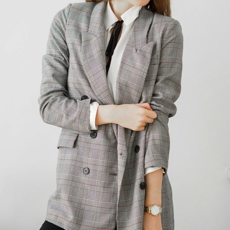 Person wearing a gray checkered blazer over a white shirt on a plain background